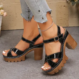 Close-up of black patent leather chunky heel sandals with cross straps and buckle strap