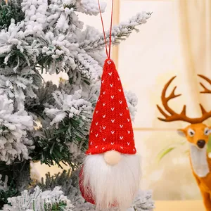 Festive red knitted Christmas gnome hanging ornament on a snowy tree for holiday decor