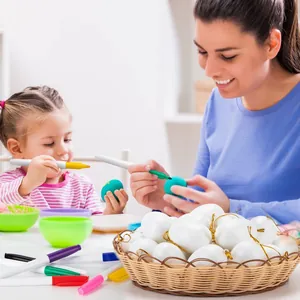 A woman and young child decorating white DIY Easter eggs with markers in a warm home