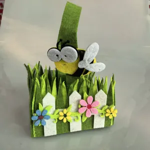 Handgefertigter Osterkorb aus Filz mit einer niedlichen Biene und bunten Blumen am Zaun