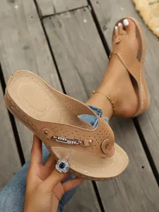 Vista detallada de chanclas de cuña beige para mujer con cadena de pedrería y calados láser