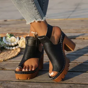 Detailed view of black chunky platform sandals with toe-loop design on wooden deck