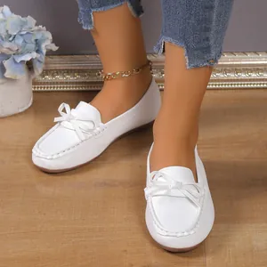 Gros plan de mocassins plats blancs vintage avec nœud décoratif sur un sol en bois clair