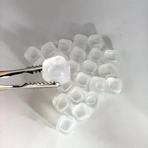 Macro shot of reusable white plastic ice cubes with metal tongs on white surface.