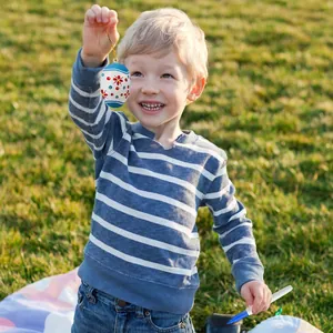 Child holding a DIY painted Easter egg with a blue floral pattern in an outdoor setting