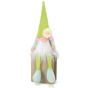 Détail d'un gnome en peluche vert assis sur un bloc de bois avec une fleur