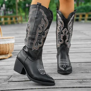 Detail of vintage black cowboy boots with intricate white embroidery on wooden deck