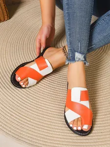 Detailansicht der flachen Sandalen in Orange und Weiß am Fuß des Models