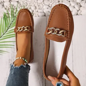 Detailed close-up of brown faux leather loafers featuring a gold-tone rhinestone chain.
