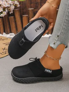 Close-up of black suede mule shoes featuring a functional toggle drawstring and branded label