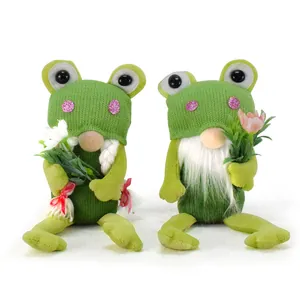Close-up view of two green knitted frog gnomes holding spring flowers for home decoration.