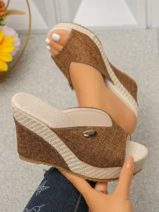 Detailopname van bruine sleehak slippers met geweven plateau en metalen logo detail.