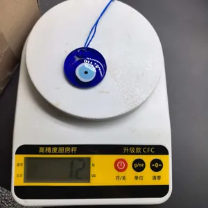 Detailed view of a blue glass Evil Eye pendant on a digital scale showing its weight is 12g.