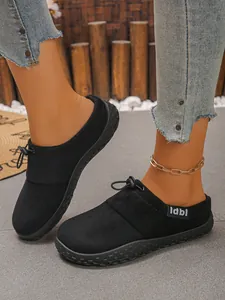 Detailed side view of black suede slip-on mules with drawstring knot decoration