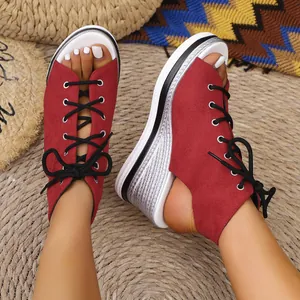 Detailed macro view of red suede peep-toe wedge sandals featuring black lace-up design