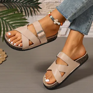 Detail view of beige cross-strap slippers featuring a cork sole and metal buckle.