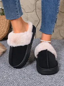Close-up of black winter slippers with plush fur lining worn on a grey carpet