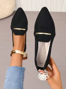 Close-up detail of black pointed-toe flat loafers with elegant gold metal bar accent.