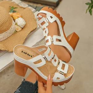 Gros plan de sandales blanches à talons compensés avec boucles dorées et lanières évidées.