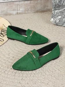 Detail of green suede pointed-toe flats with gold metal bar accent on textured rug