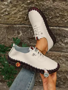 Detalle de zapatos planos casuales de cuero blanco para mujer con costuras negras a mano