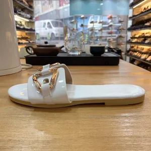 Primo piano laterale di sandalo piatto in vernice bianca con fibbia dorata decorativa.