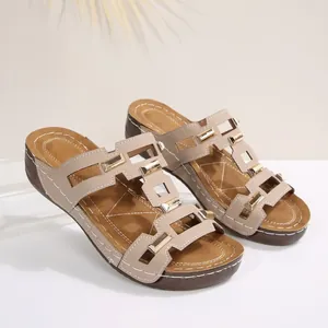 Detailansicht von Keilsandalen für Damen mit geometrischen Goldschnallen und braunen Riemen.