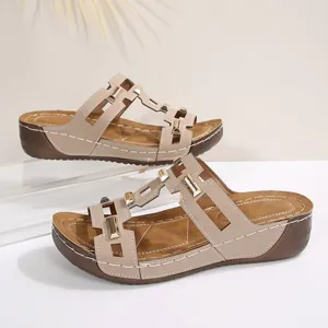 Seitenansicht beiger Keilsandalen mit dekorativen geometrischen Goldschnallen und weißen Nähten.