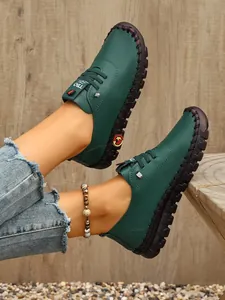 Primer plano de mocasines planos de cuero verde cosidos a mano para mujer en madera