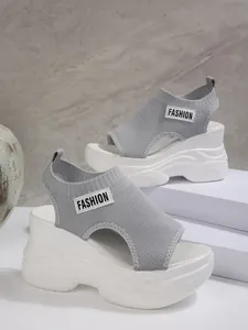 Detailopname van grijze gebreide platformsandalen met wit 'FASHION' patchdetail.