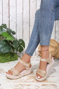 A detailed view of stylish beige wedge sandals with buckle straps worn by a model