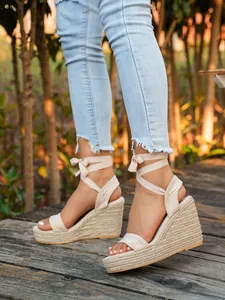 Close-up view of beige suede lace-up espadrille wedge sandals worn on wooden deck