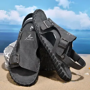 Close-up detail of dark grey men's beach sandals with double buckles on a sunny sandy shore.