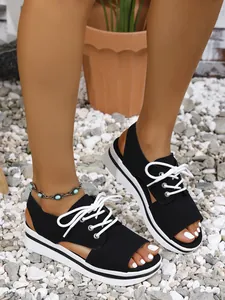Detail view of women's black platform open-toe sandals with white laces on gravel