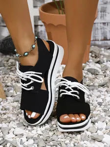 Detail view of women's black platform sandals with white laces on a natural pebble surface