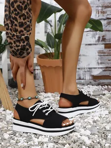 Detailed view of black platform peep-toe sandals with white laces on outdoor white pebbles