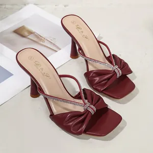 Primo piano di sandali bordeaux con fiocco e cinturini di strass scintillanti e punta quadra.