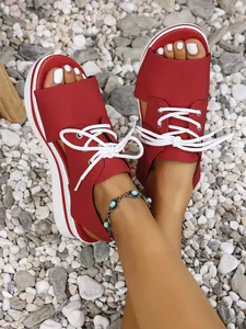 Detail view of stylish red platform peep-toe sandals with white laces on beach pebbles