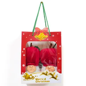 Close-up of two cute apple-themed Christmas gnomes inside a festive red gift bag.