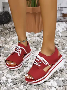 Close-up detail of red platform lace-up sandals worn by a model on white gravel