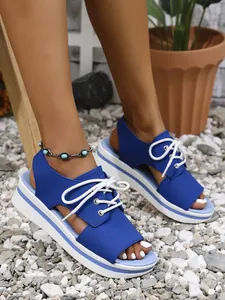 Detailed view of blue platform sandals with white lace-up design on a gravel surface