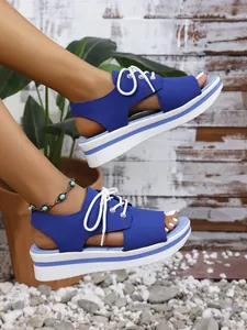 Close-up detail of blue platform peep-toe sandals with white laces on female model's feet.