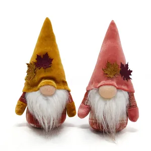 Close-up of two fall harvest gnomes with maple leaf decorations and soft velvet hats.