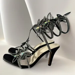 Seitenansicht eleganter schwarzer High-Heel-Sandalen mit Strass und Schmetterling.