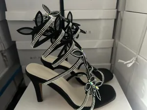 Detailaufnahme schwarzer High-Heel-Sandalen mit Strass-Schleife und Wickelriemen