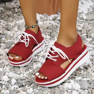 Detailed side view of women's red peep-toe platform sandals with white laces on pebbles.