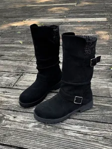 Detailopname van zwarte suède slouch laarzen met gebreide kraag en decoratieve gespen