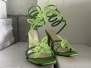 Detailansicht grüner High-Heel-Sandalen mit Strassschmetterling und Spiralriemen.