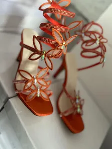Detail der orangefarbenen Sandalen mit Strass-Schmetterling und Wickelriemen