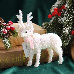 Detail eines weißen schimmernden Weihnachts-Elch-Ornaments mit rosa Schleife auf Büchern.